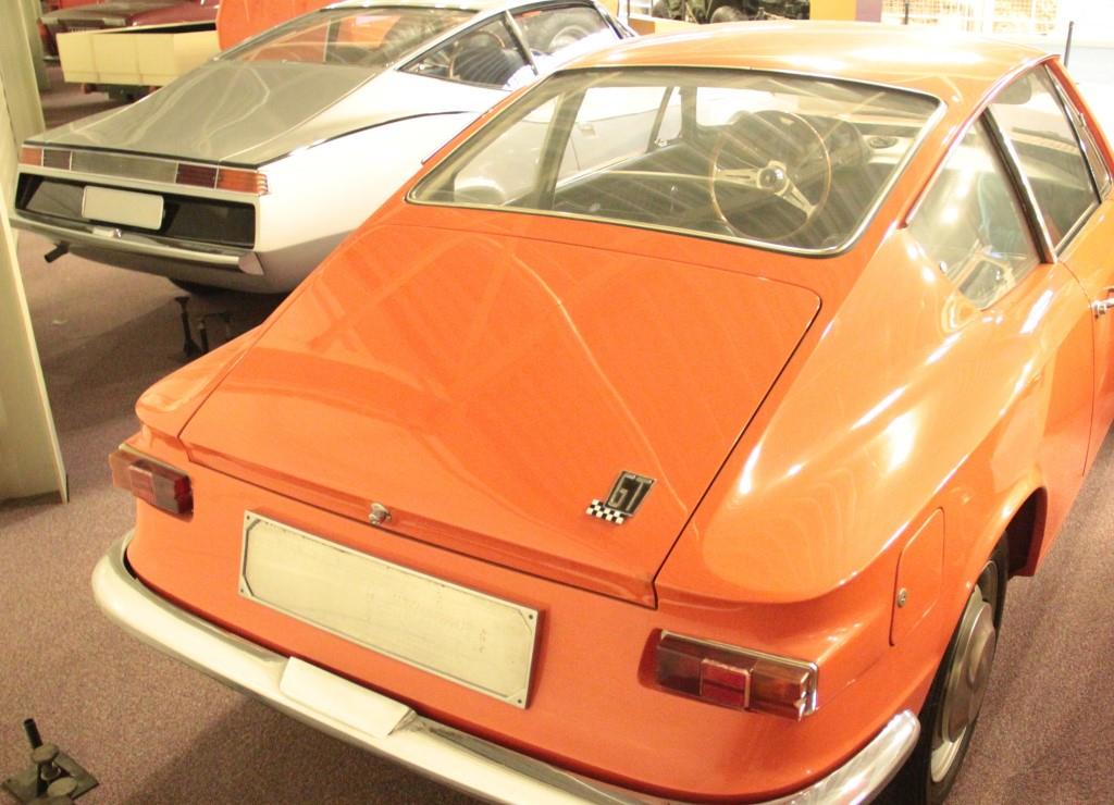 Een zilvergrijze en oranje coupé schuin van achter gezien.