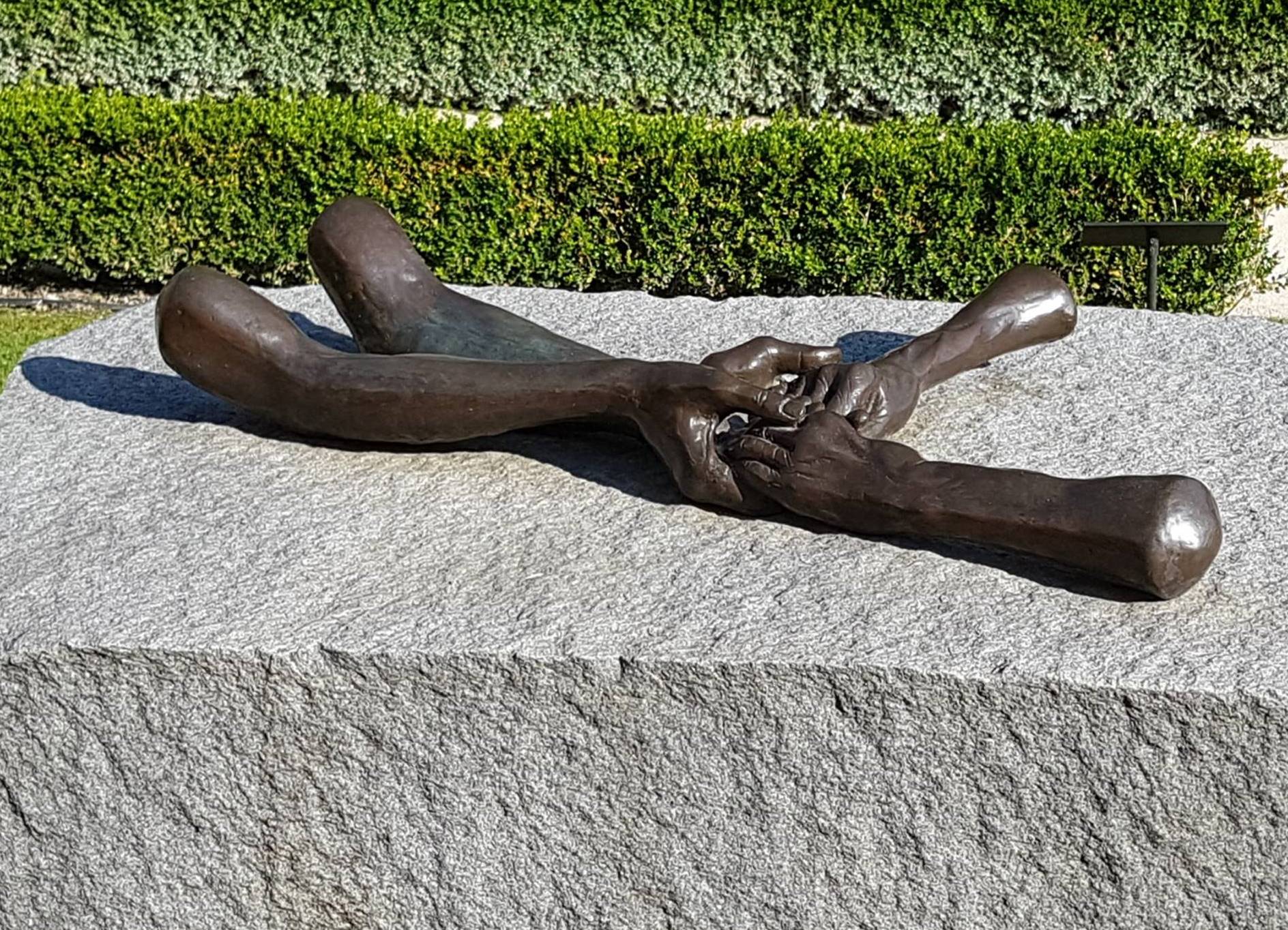 Bronze hands with forearms on granite block.